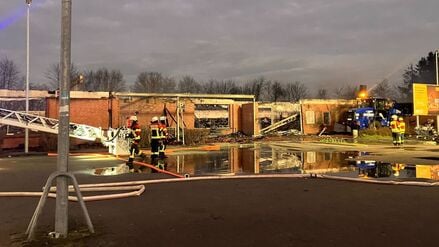 Feuerwehrleute stehen bei den Nachlöscharbeiten zu einem Brand vor zerstörten Gebäuden. 