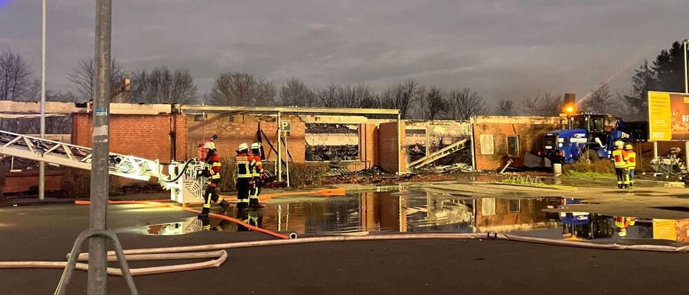 Feuerwehrleute stehen bei den Nachlöscharbeiten zu einem Brand vor zerstörten Gebäuden. 
