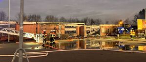 Feuerwehrleute stehen bei den Nachlöscharbeiten zu einem Brand vor zerstörten Gebäuden. 