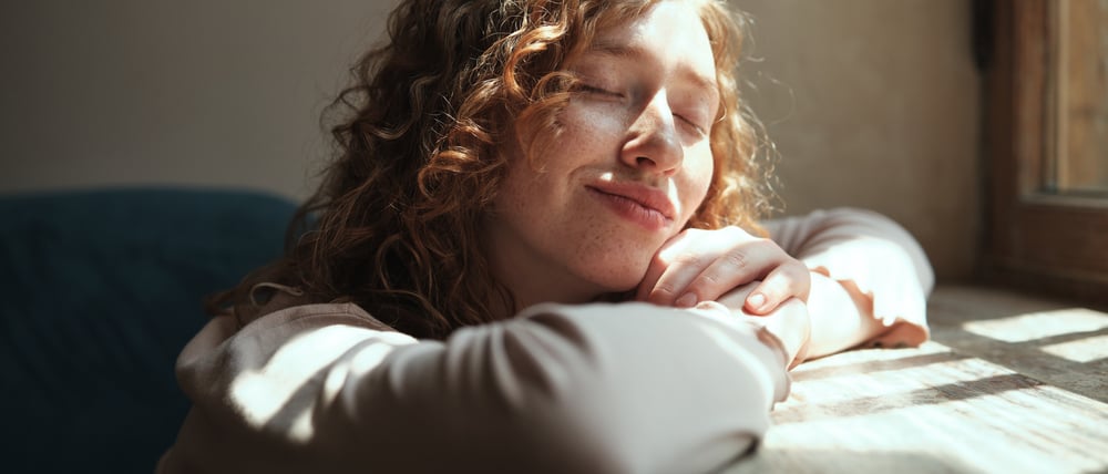 Eine junge Frau genießt Sonnenlicht, das durch ein Fenster fällt.