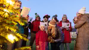 Eine Gruppe von Menschen singt draußen an einem Weihnachtsbaum Lieder.