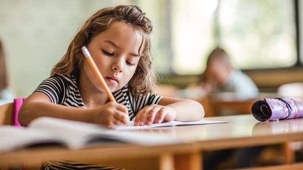 Ein Kind sitzt mit einem Stift in der Hand an einem Schultisch.