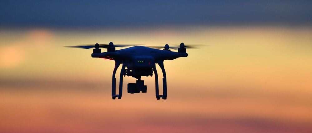 Eine Drohne fliegt bei Sonnenuntergang über eine Wiese.