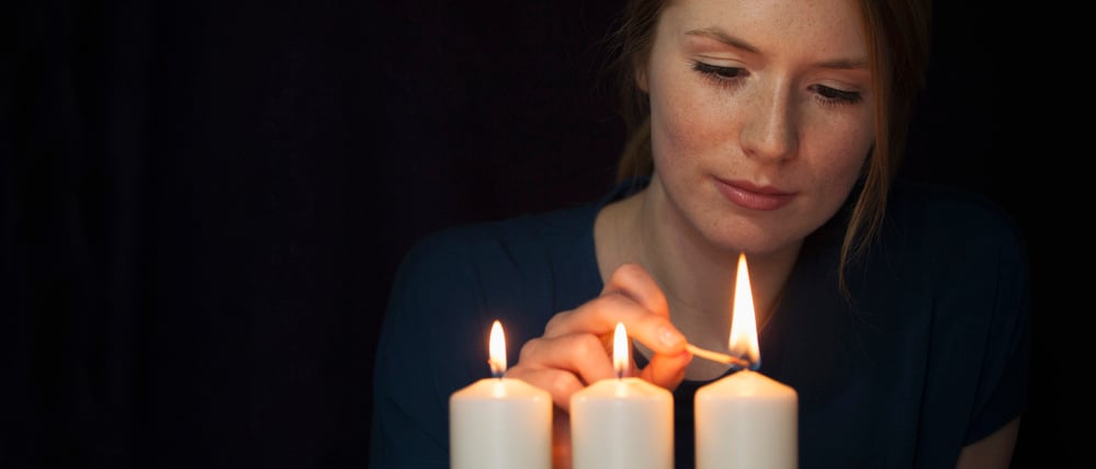 Illustration: Eine Frau zündet drei Kerzen mit einem Streichholz an.