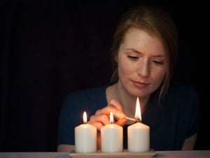 Illustration: Eine Frau zündet drei Kerzen mit einem Streichholz an.