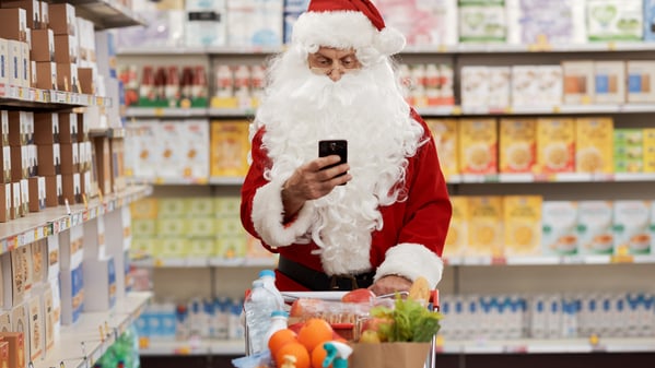 Ein Weihnachtsmann schiebt einen Einkaufswagen durch einen Supermarkt.