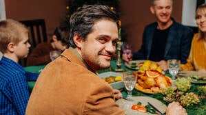 Symbolfoto: Ein Mann sitzt mit Freunden und Freundinnen am gedeckten Tisch
