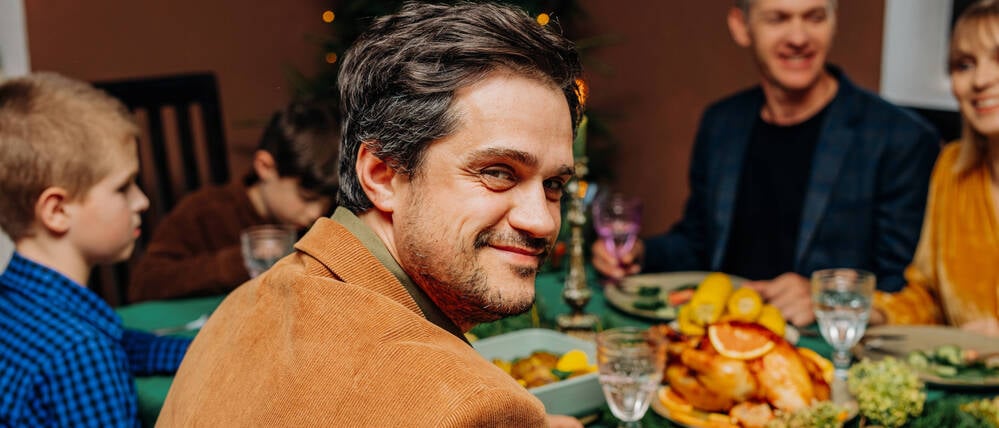 Symbolfoto: Ein Mann sitzt mit Freunden und Freundinnen am gedeckten Tisch