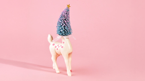Pastel holiday scene with deer figure with Christmas tree head on pink background. Room for copy.