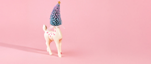 Pastel holiday scene with deer figure with Christmas tree head on pink background. Room for copy.