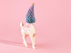 Pastel holiday scene with deer figure with Christmas tree head on pink background. Room for copy.