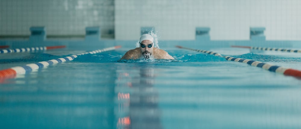 Mid adult man swimming freestyle in pool lane.