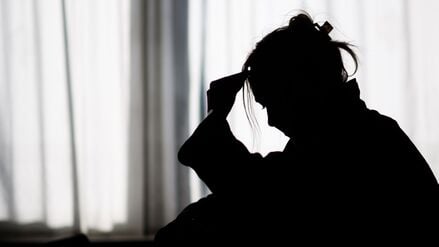 Die Silhouette einer Frau zeichnet sich vor einer hellen Fensterfront ab.