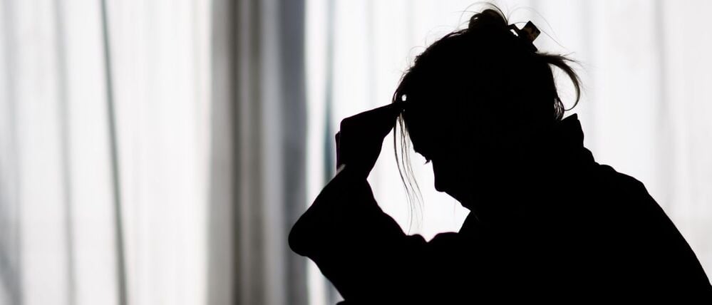 Die Silhouette einer Frau zeichnet sich vor einer hellen Fensterfront ab.