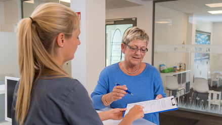 Eine Patientin reicht einer Arzthelferin einen Anamnesebogen.