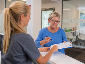 Eine Patientin reicht einer Arzthelferin einen Anamnesebogen.