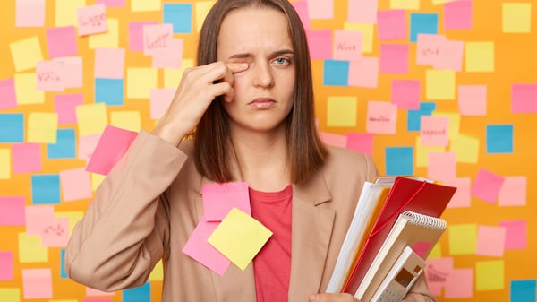 Eine Frau, beklebt mit Post-Its, reibt sich müde ihr Auge.
