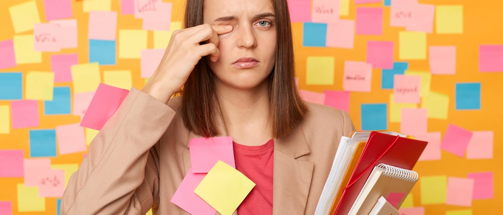 Eine Frau, beklebt mit Post-Its, reibt sich müde ihr Auge.