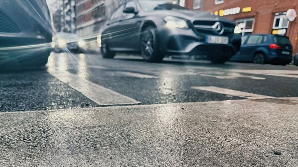 Das Licht der Fahrzeuge an einer Ampel bricht sich im Asphalt einer Straße. Blitzeis verwandelte besonders die Gehwege in Rutschbahnen.