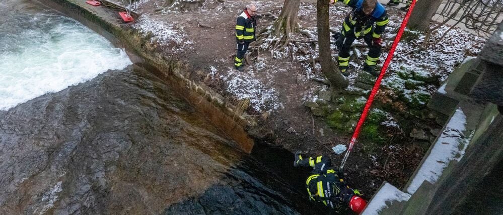 Mitarbeiter der Berufsfeuerwehr bauen in Anwesenheit von Polizeibeamten die diversen Einbauten und Vorrichtungen für eine künstliche Welle am Eisbach wieder ab.