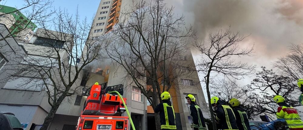 Einsatzfahrzeuge von Rettungskräften und Feuerwehr stehen vor einem Hochhaus, aus dem Rauch aufsteigt. In Berlin-Spandau brennt seit den frühen Morgenstunden ein Hochhaus. 