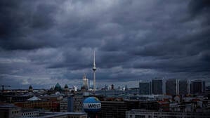 Dunkle Wolken ziehen über Berlin, während der Fernsehturm von einem Sonnenstrahl getroffen wird.