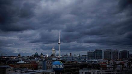 Dunkle Wolken ziehen über Berlin, während der Fernsehturm von einem Sonnenstrahl getroffen wird. 