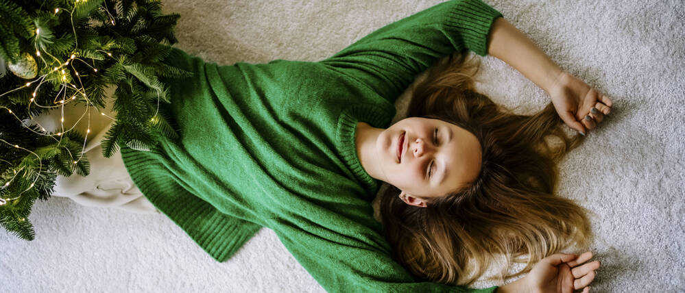 Ein Mädchen liegt mit geschlossenen Augen neben ihrem Weihnachtsbaum. 
