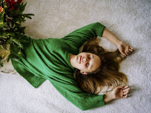 Ein Mädchen liegt mit geschlossenen Augen neben ihrem Weihnachtsbaum. 
