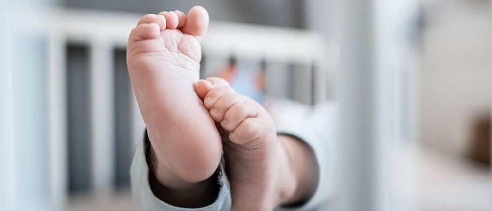 Die Füße eines Babys sind in einem Kinderbett zu sehen.