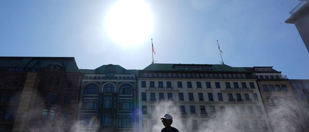Kinder und Passanten gehen durch einen Sprühnebel eines Wasserzerstäubers am Jungfernstieg in der Innenstadt.