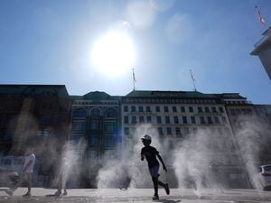 Kinder und Passanten gehen durch einen Sprühnebel eines Wasserzerstäubers am Jungfernstieg in der Innenstadt.