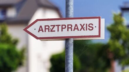 Ein Schild mit der Aufschrift „Arztpraxis“ steht an der Straße. (Symbolbild)