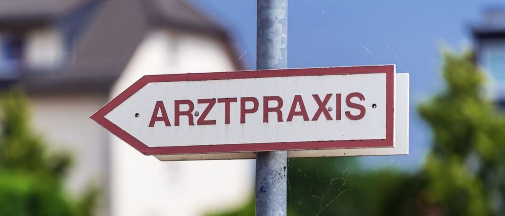 Ein Schild mit der Aufschrift „Arztpraxis“ steht an der Straße. (Symbolbild)