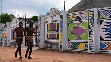 Junge Männer vom Volk der Ndebele laufen am Haus von Esther Mahlangu, einer zeitgenössischen südafrikanischen Künstlerin, in KwaMhlanga in Mpumalanga, Südafrika, vorbei. 