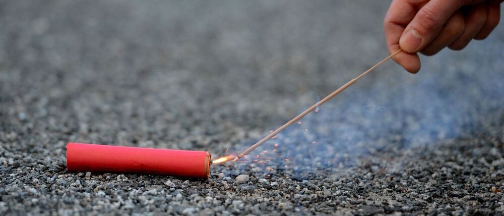 Der Bildausschnitt zeigt eine Hand, die einen Böller anzündet.