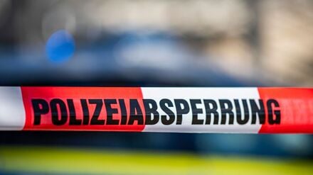Ein Absperrband mit der Aufschrift Polizeiabsperrung ist vor einem Polizeiwagen aufgespannt. 