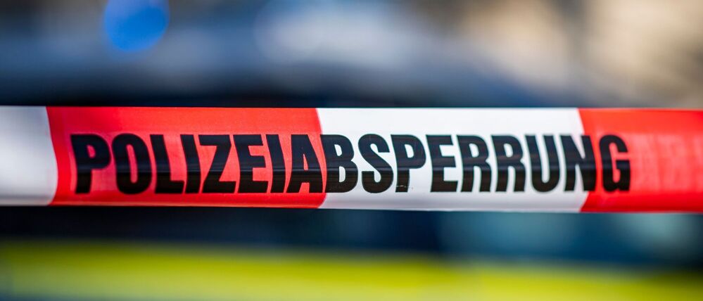 Ein Absperrband mit der Aufschrift Polizeiabsperrung ist vor einem Polizeiwagen aufgespannt. 