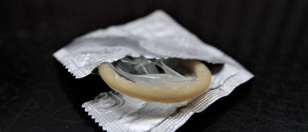 Eine geöffnete Kondompackung liegt neben einem Bett auf einem Nachttisch. (Symbolfoto)