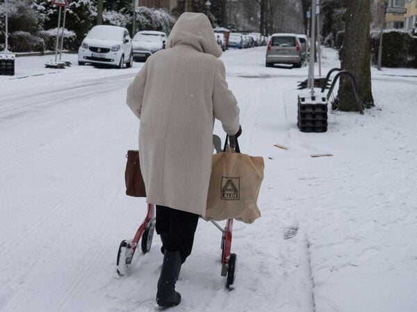 03.01.2026, Berlin: Eine ältere Frau geht mit ihrem Rollator über Schnee auf einer Straße in Lichterfelde. Die Seniorin trägt ihre Einkäufe nach Hause. Bei winterlicher Witterung sind im Südwesten von Berlin viele Haushalte von einem Stromausfall betroffen. Foto: Wolfram Steinberg/dpa +++ dpa-Bildfunk +++