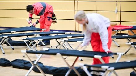 03.01.2026, Berlin: Ehrenamtliche Mitarbeiter des DRK bauen während des Stromausfalls im Südwesten Berlins in einer Notunterkunft Feldbetten auf. 