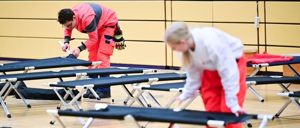 03.01.2026, Berlin: Ehrenamtliche Mitarbeiter des DRK bauen während des Stromausfalls im Südwesten Berlins in einer Notunterkunft Feldbetten auf.