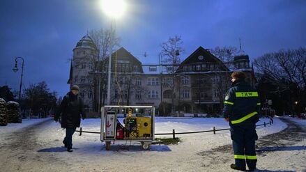 Ein Mitarbeiter (r) des Technischen Hilfswerks (THW) steht während eines Stromausfalls im Südwesten Berlins am Mexikoplatz an einer Lichtsäule. 