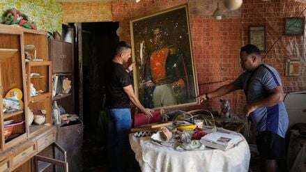 Jesus Linares (r.) entfernt ein Gemälde des Unabhängigkeitshelden Simón Bolívar in seinem Haus, das seiner Aussage nach während der US-Militäroperationen zur Festnahme des venezolanischen Präsidenten Maduro getroffen wurde.