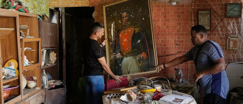 Jesus Linares (r.) entfernt ein Gemälde des Unabhängigkeitshelden Simón Bolívar in seinem Haus, das seiner Aussage nach während der US-Militäroperationen zur Festnahme des venezolanischen Präsidenten Maduro getroffen wurde.