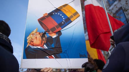 Pro‑Nicolás‑Maduro‑Kundgebung vor der US‑Botschaft in Madrid: Ein Demonstrant hält ein Banner mit einer Karikatur von Donald Trump, der venezolanisches Öl trinkt.