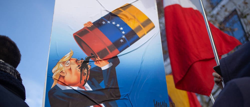 Pro‑Nicolás‑Maduro‑Kundgebung vor der US‑Botschaft in Madrid: Ein Demonstrant hält ein Banner mit einer Karikatur von Donald Trump, der venezolanisches Öl trinkt. 
