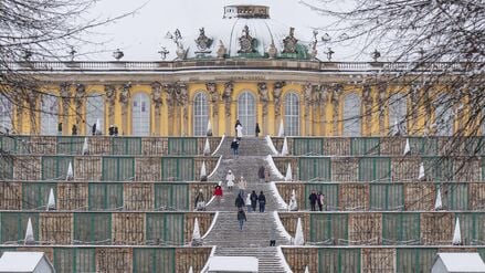 Menschen gehen vor der verschneiten Kulisse des Schloss Sanssouci in Potsdam spazieren.