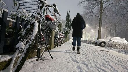 Eine Frau geht bei Schneetreiben an einem zugeschneiten Fahrrad vorbei.