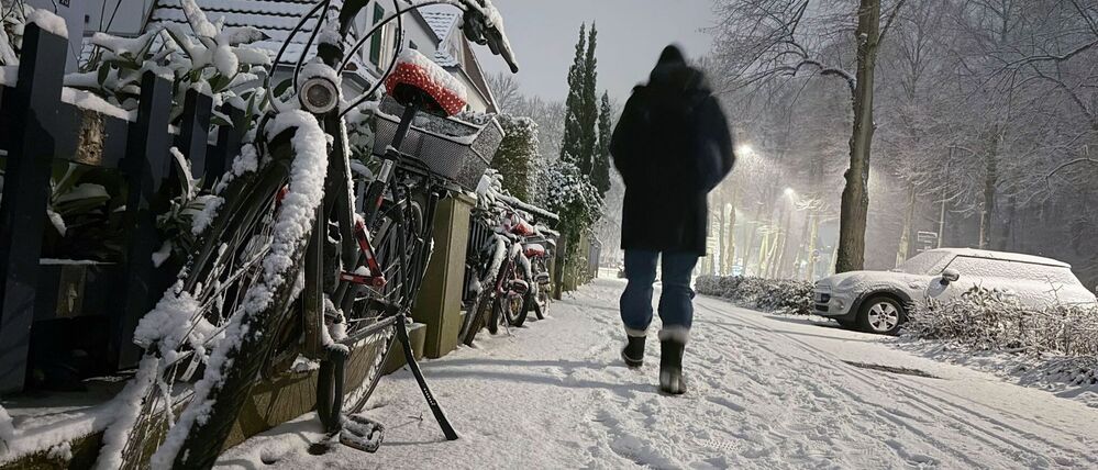 Eine Frau geht bei Schneetreiben an einem zugeschneiten Fahrrad vorbei.